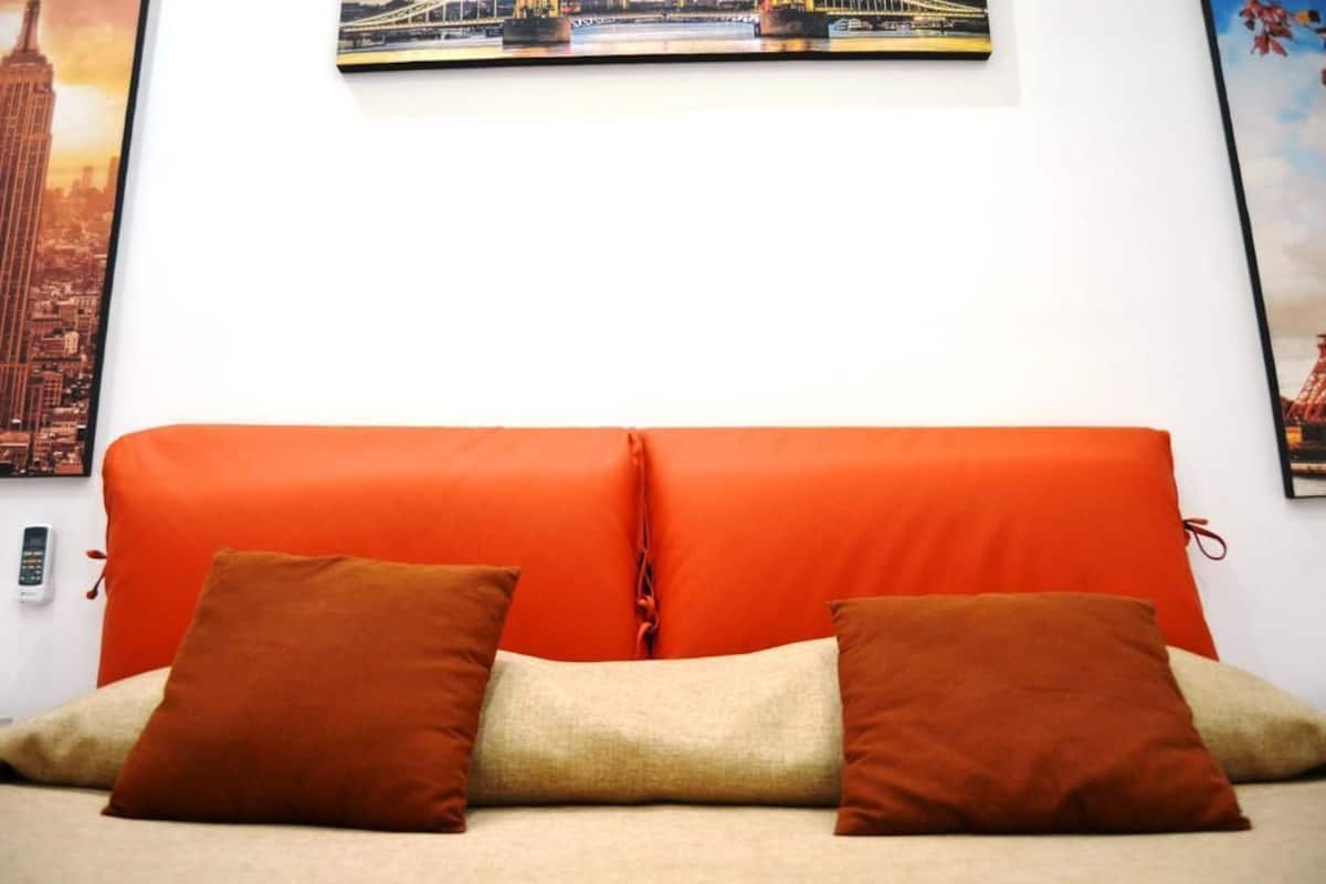 A room with a red sofa, two brown pillows, and a beige pillow.