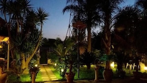 A nighttime garden pathway with palm trees and potted plants, leading to a building entrance. - Beatrice Home B&B (Pompei)