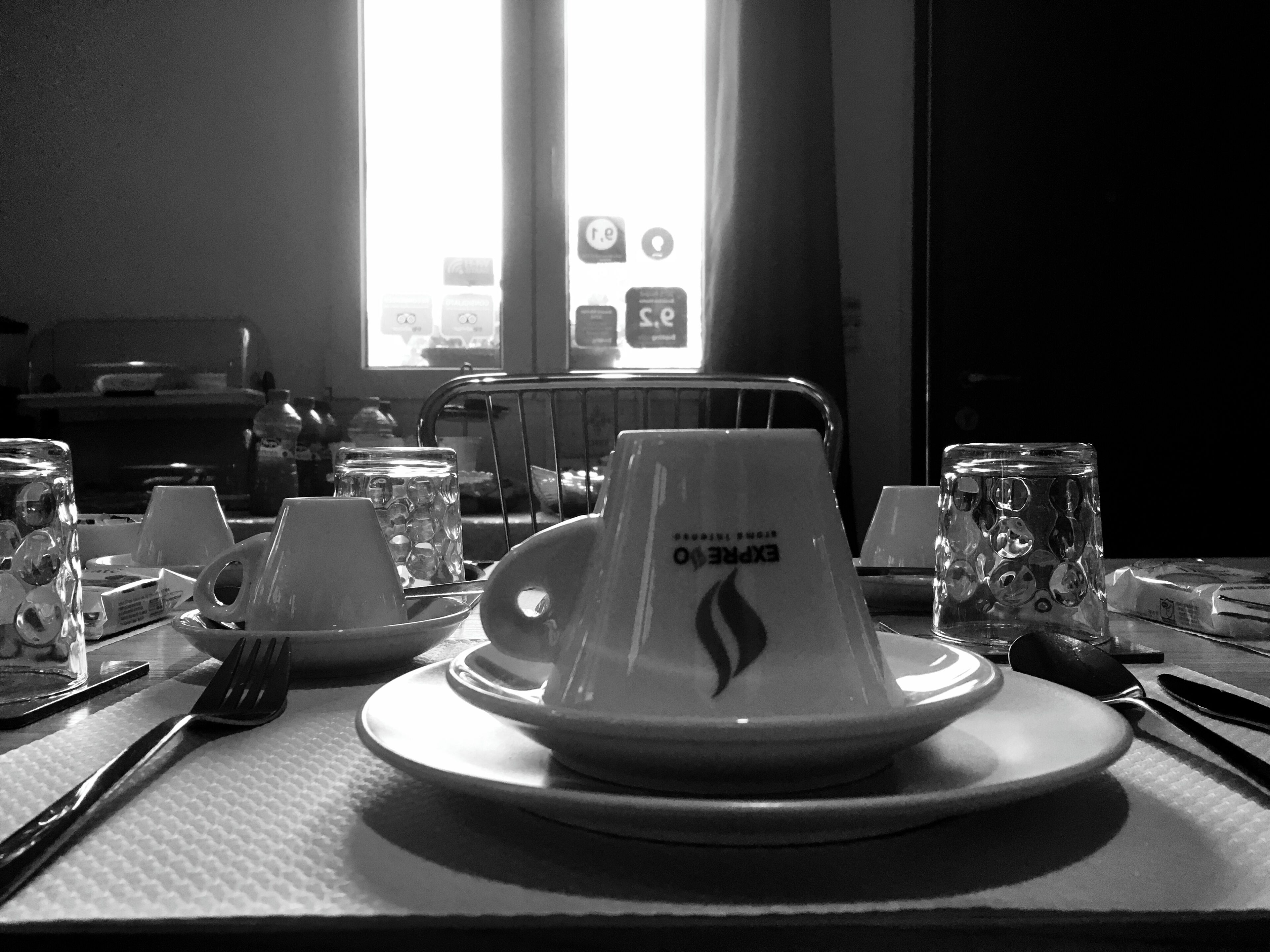 Mesa de comedor dispuesta con platos, vasos y cubiertos en una habitación con una ventana al fondo.