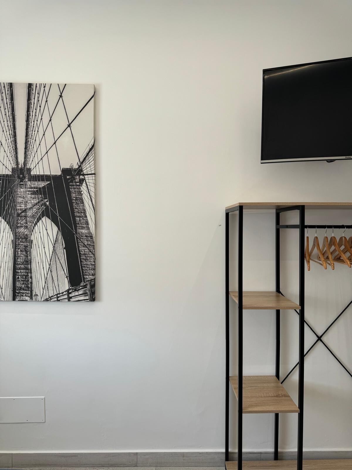 A room with a black and white abstract painting, a mounted television, and a wooden shelving unit with hooks.