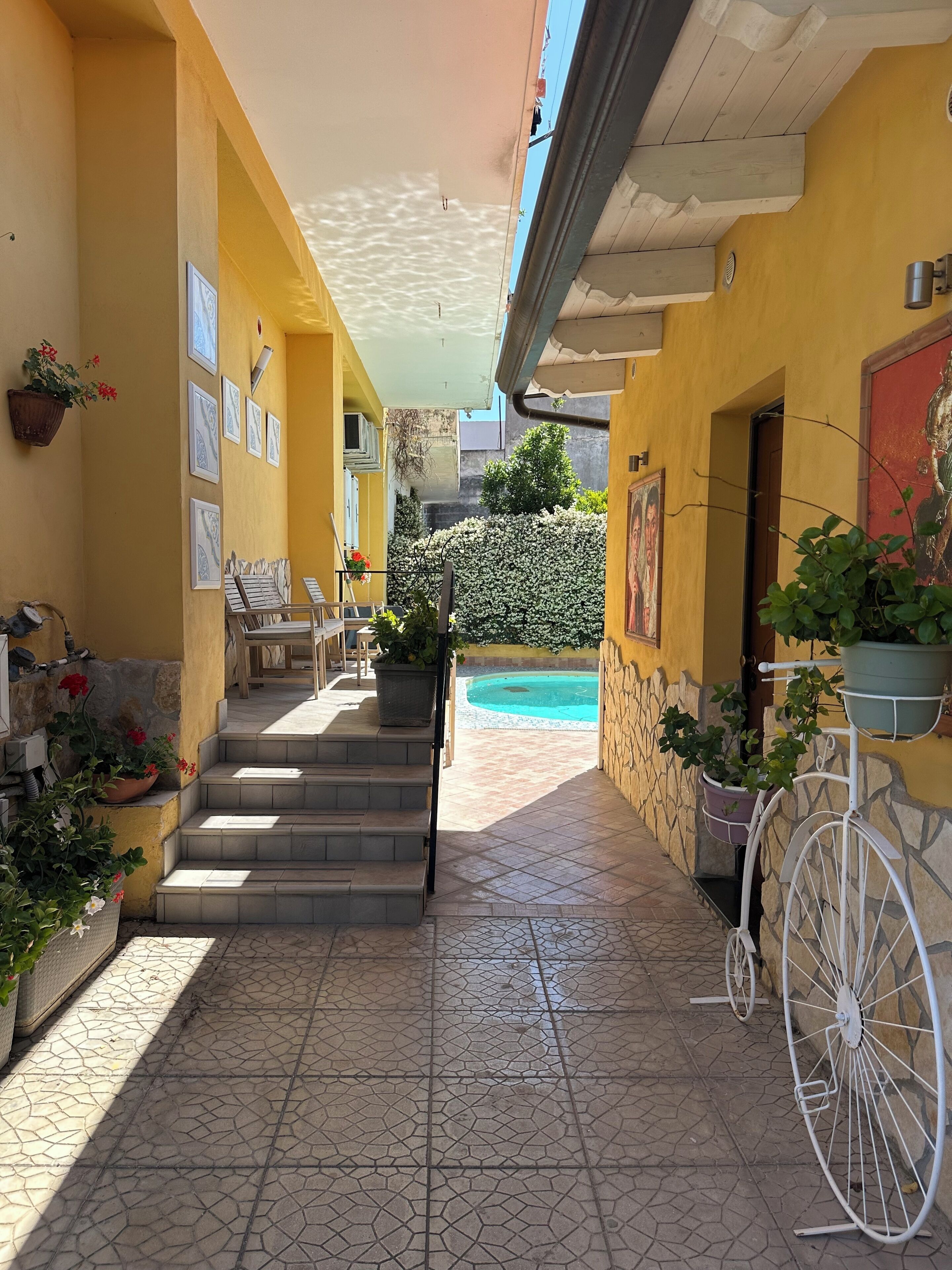 A covered outdoor area with tiled flooring, a staircase leading to a pool, and potted plants.