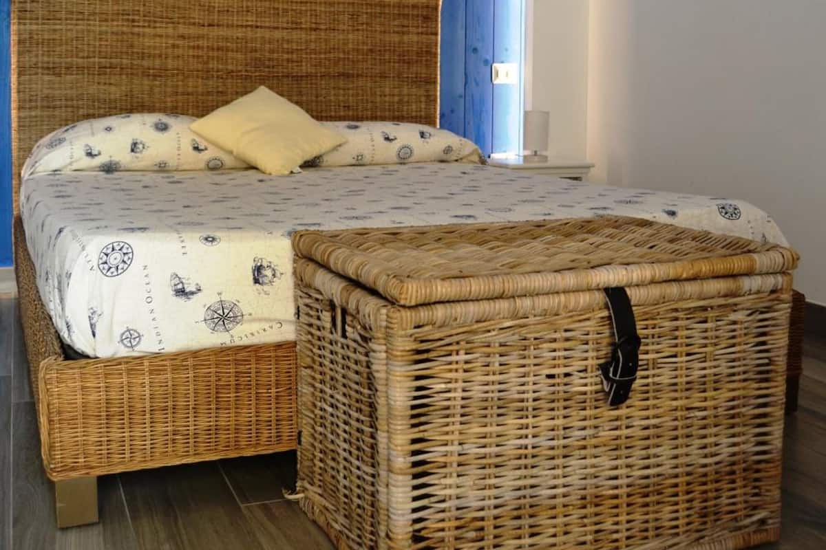 A room with a bed, a wicker chest, and a painting on the wall.