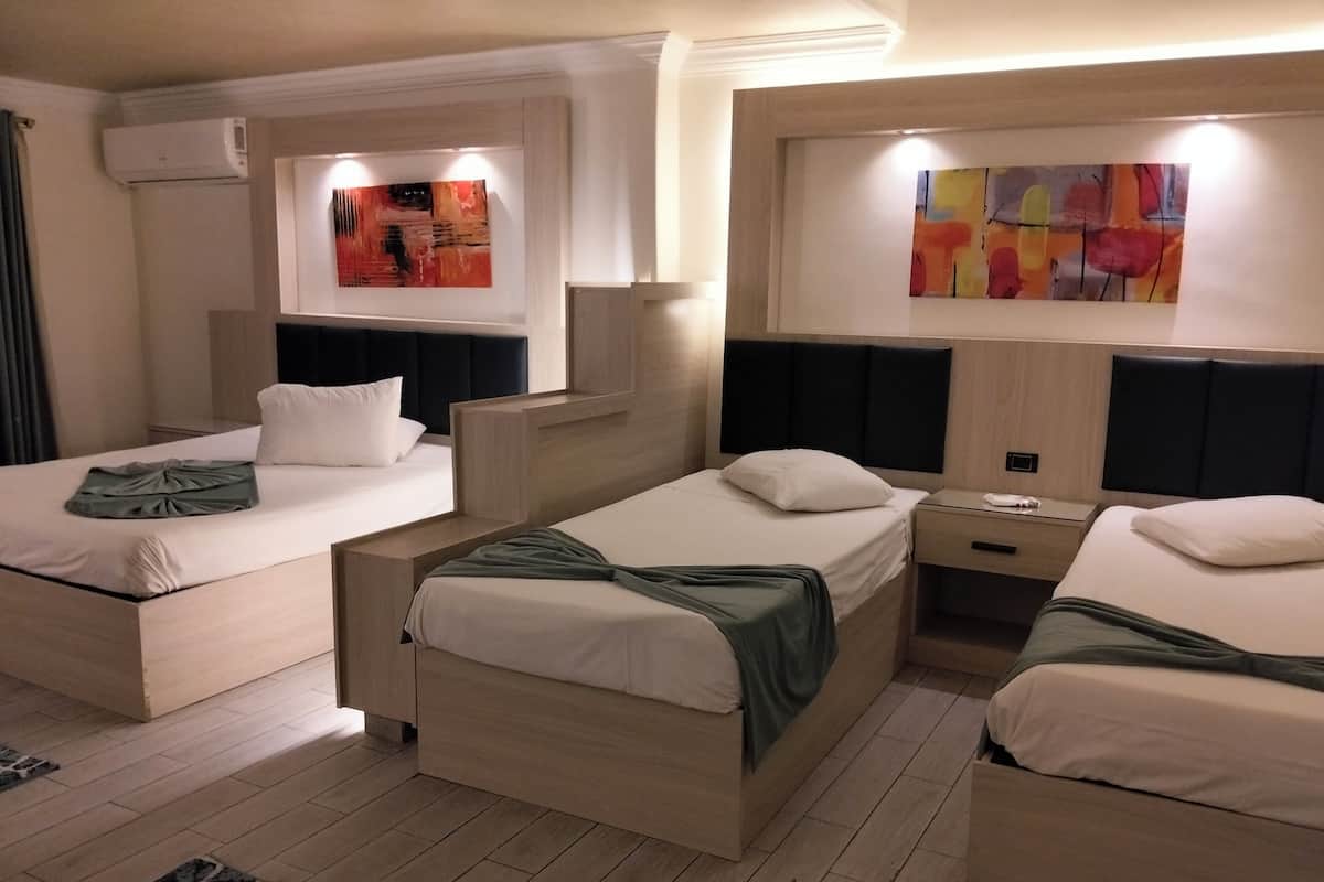 Une chambre d’hôtel avec deux lits, une table de chevet, un climatiseur fixé au mur et des œuvres d’art abstrait accrochées aux murs.