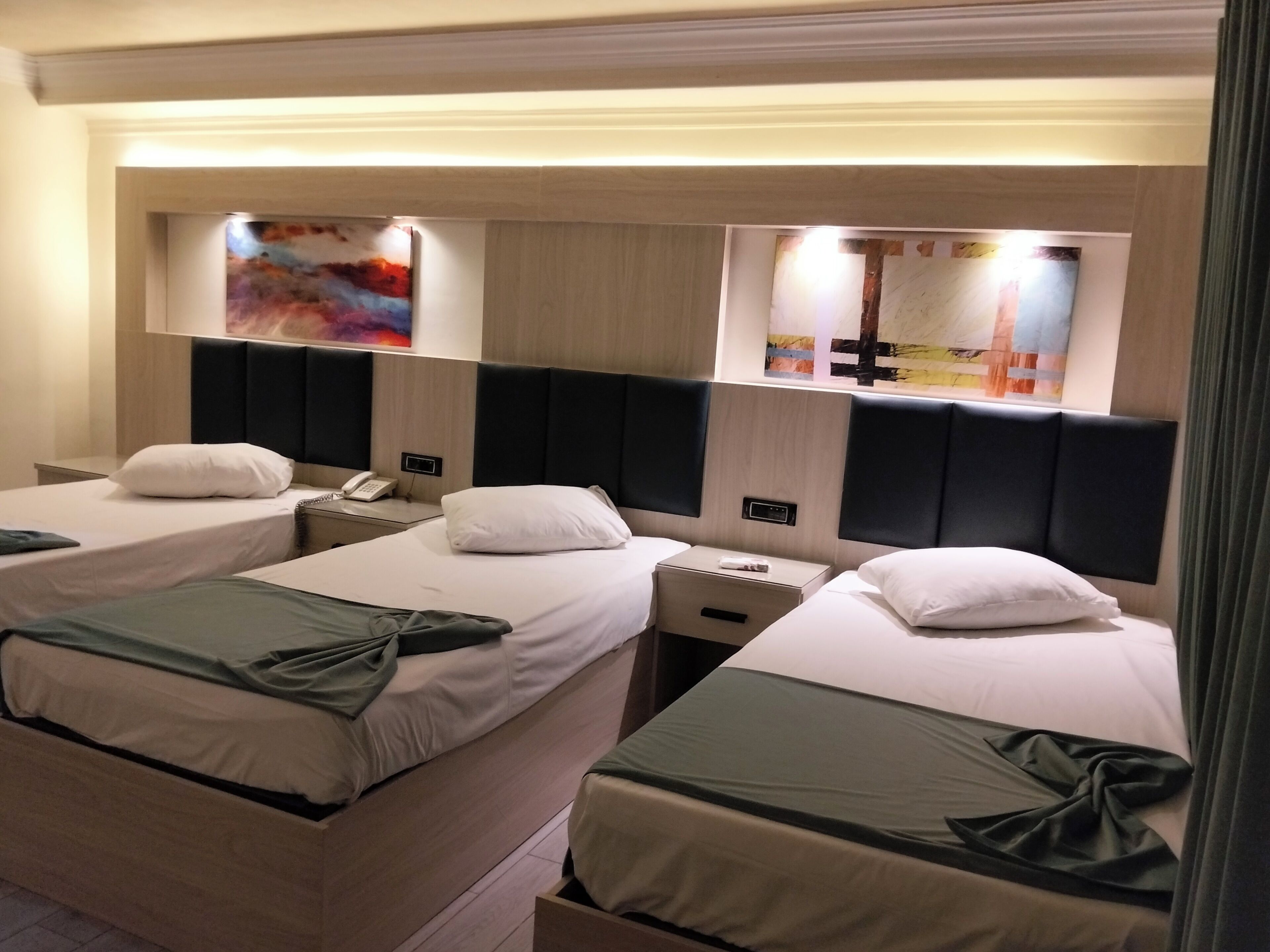 Une chambre d’hôtel avec trois lits simples, chacun étant équipé d’un oreiller et d’une table de chevet avec un téléphone.