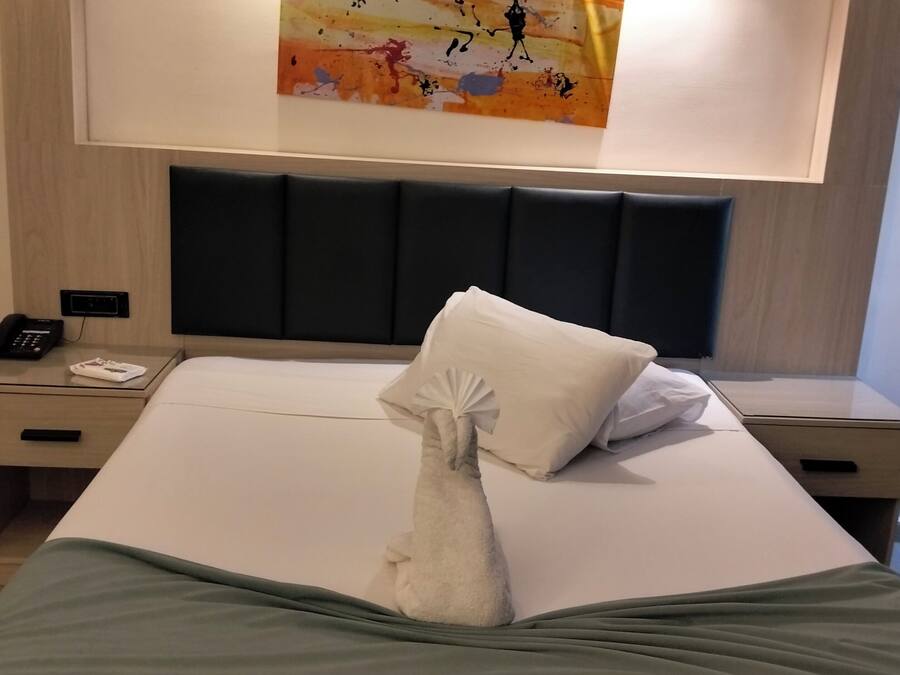 Een hotelkamer met een net opgemaakt bed, een aan de muur hangend kunstwerk en een nachtkastje met een telefoon en een afstandsbediening.