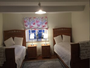 Un dormitorio con dos camas individuales, cabeceros de madera, mesitas de noche con lámparas, una cortina floral y una ventana con vistas.