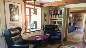 Una habitación con dos sillones de cuero, una mesa de madera, una estantería y un cuadro en la pared.