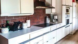 Una cocina con alacenas blancas, salpicadero de ladrillo, estufa y refrigerador.