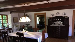 Un comedor con una mesa preparada para cuatro personas, rodeada de sillas de madera. Una lámpara colgante proporciona iluminación. Se ve un aparador con cristalería al fondo.