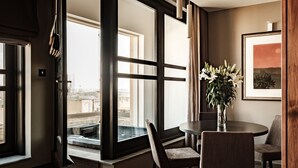 Ein modernes Hotelzimmer mit einem großen Fenster, einem Essbereich mit rundem Tisch und Stühlen sowie einem gerahmten Bild an der Wand.
