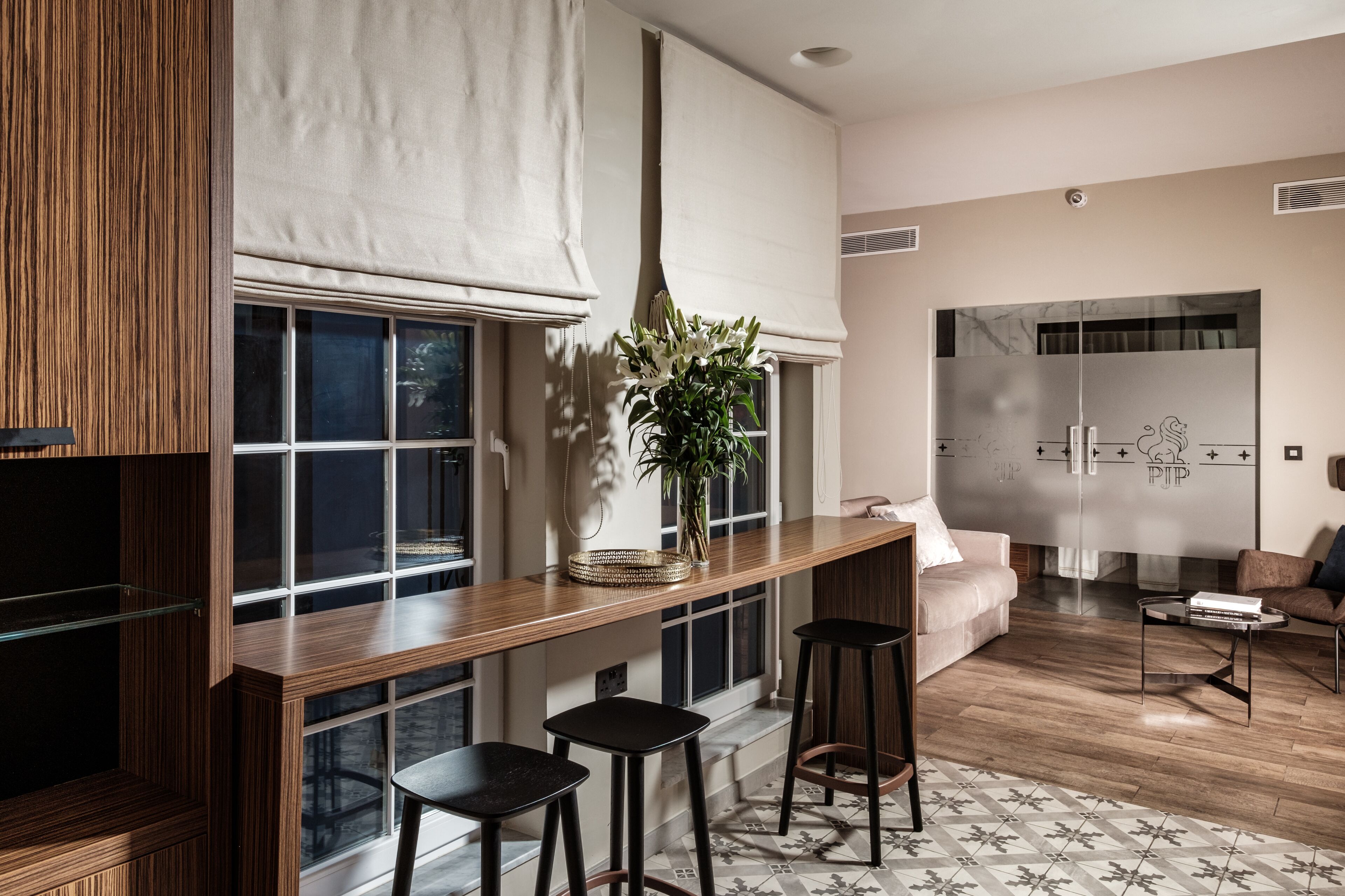 A modern kitchen with a wooden countertop, three bar stools, a vase with flowers, and a large window with a view of the outside.