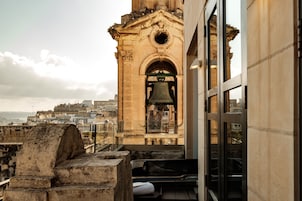 Un clocher abritant une grande cloche, un escalier en pierre et une vue sur le paysage urbain en arrière-plan.