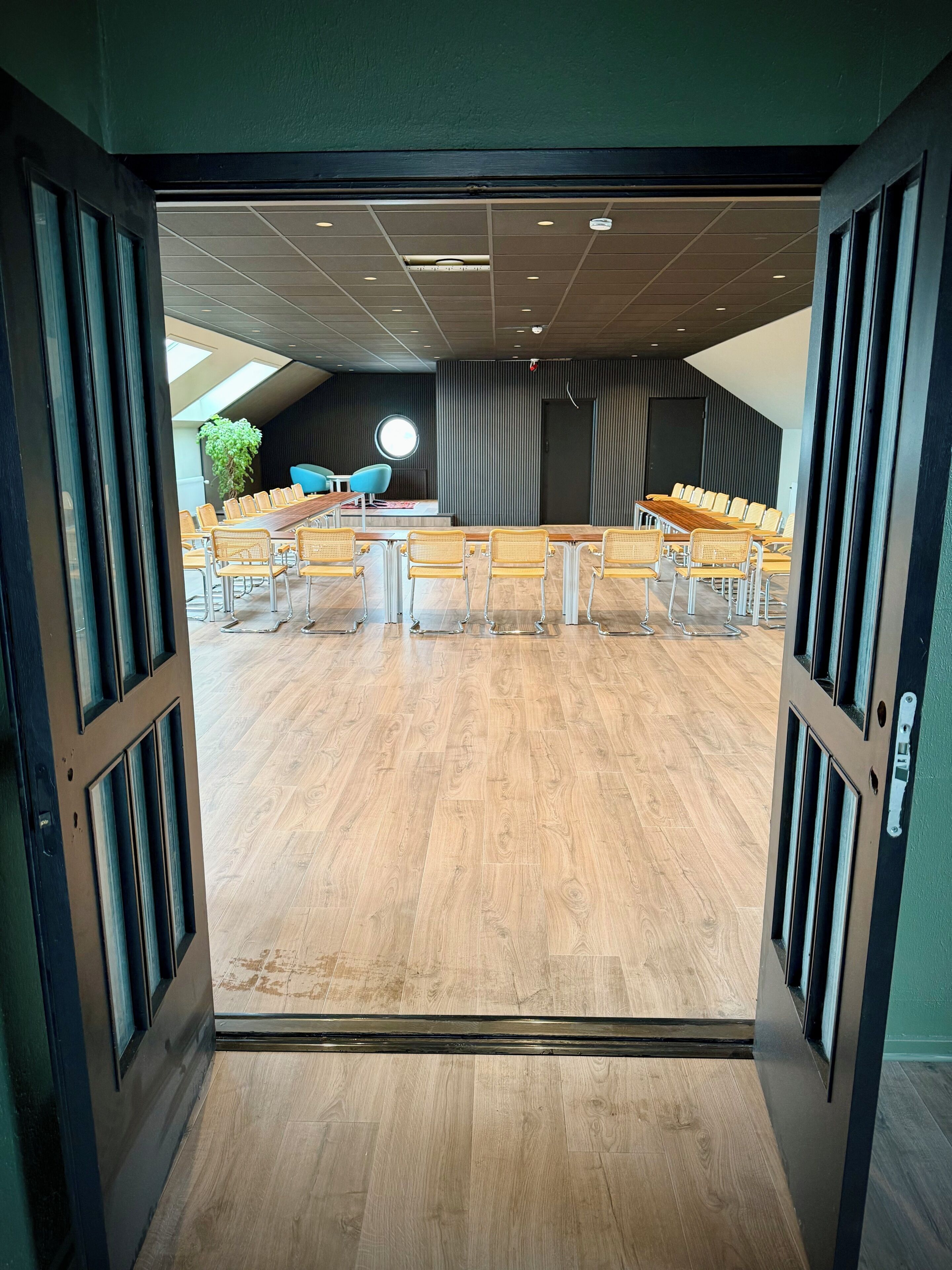 Ett konferensrum med ett långt bord och stolar, en krukväxt och ett runt fönster.