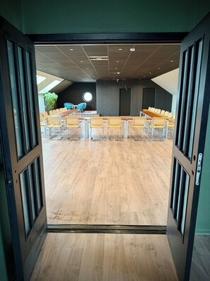 Ein Konferenzraum mit langem Tisch, Stühlen, einer Zimmerpflanze und einem Rundfenster.
