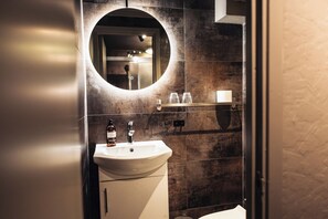 Un baño con un espejo redondo, un lavabo y una repisa con vasos.