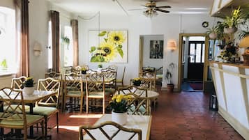 Enjoy meals in this elegant dining area with round tables and chairs, a large sunflower painting, and a framed portrait.