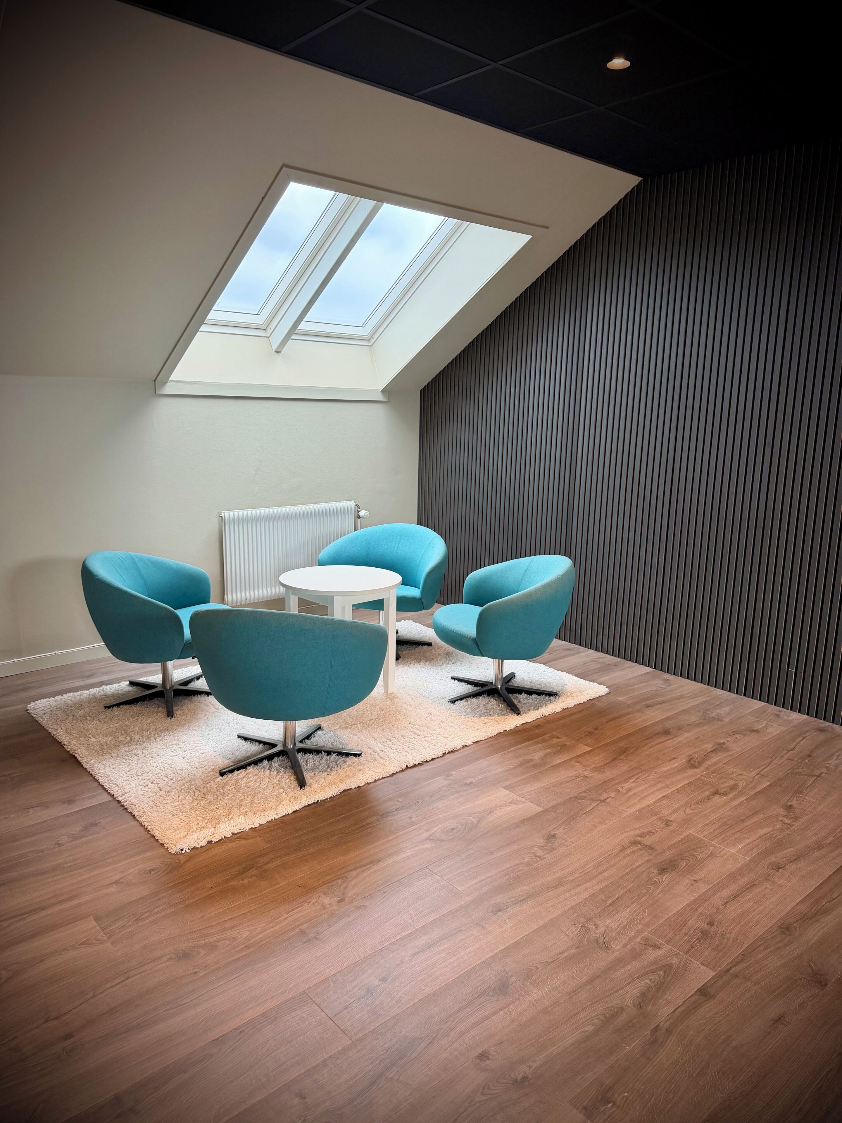 A modern room with a skylight, a round table, and four blue chairs.