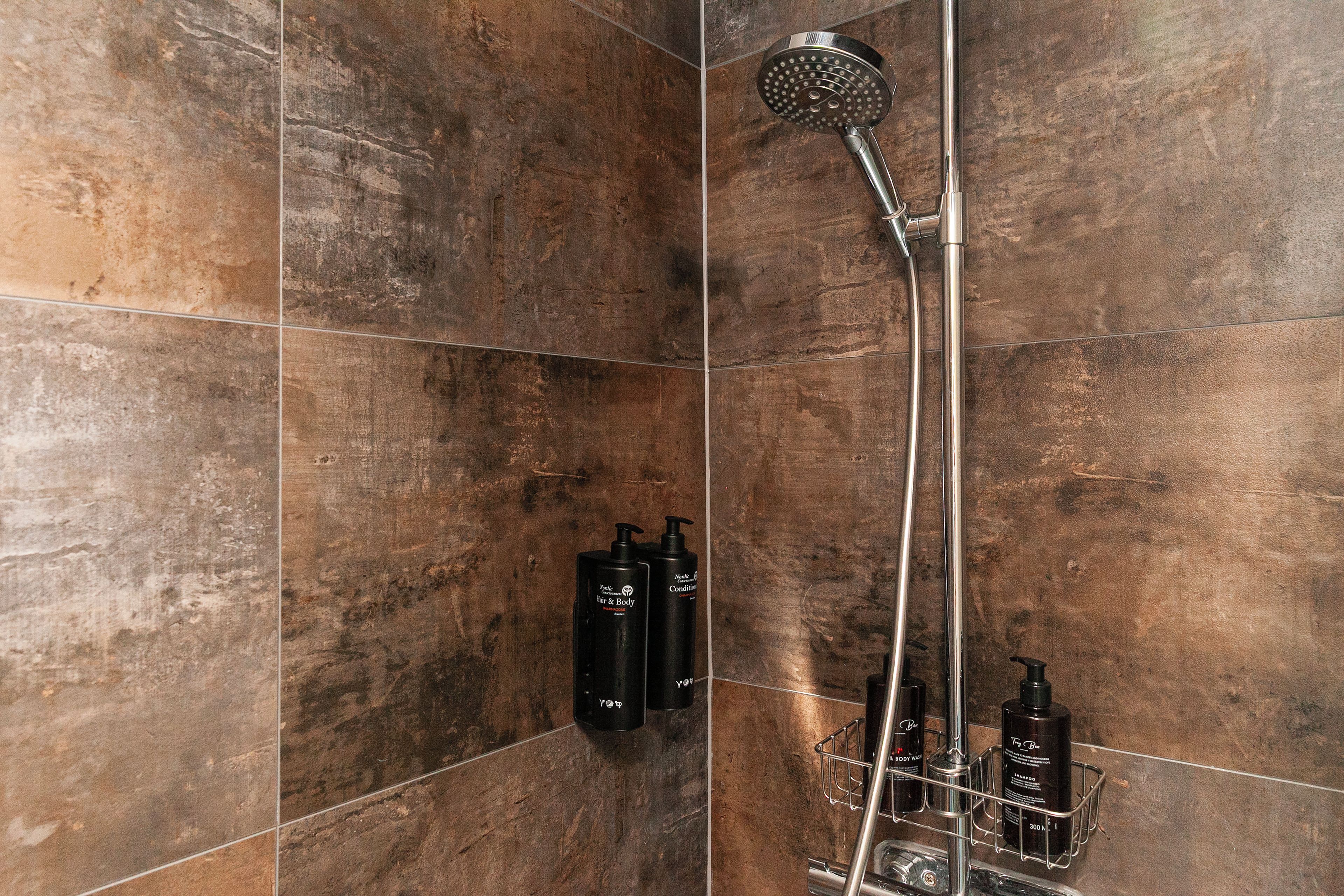Ein Badezimmer mit Dusche, gefliesten Wänden und einem Metallregal mit Flaschen.
