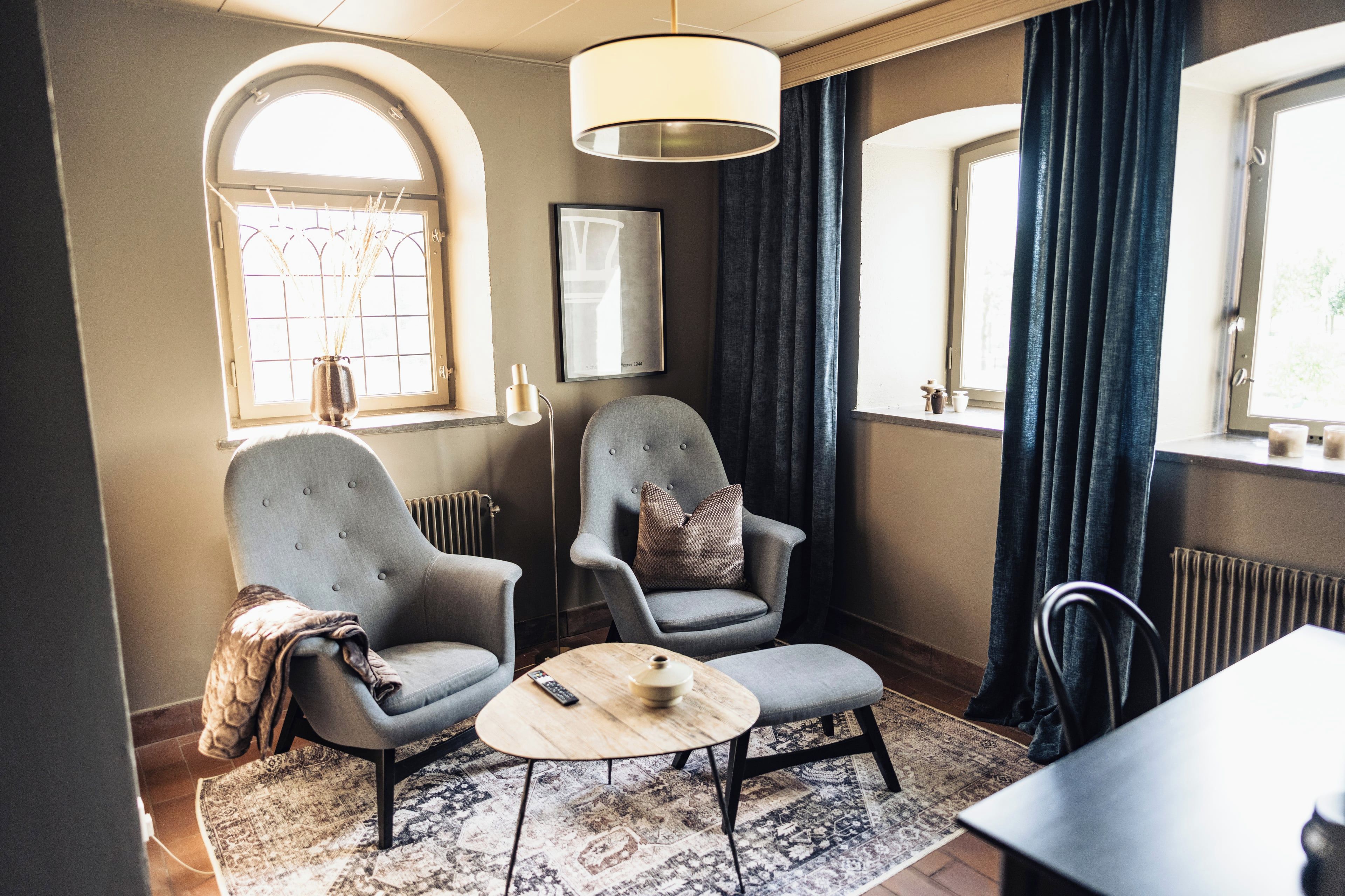 A room with two armchairs, a small round table, a radiator, and a window with curtains.