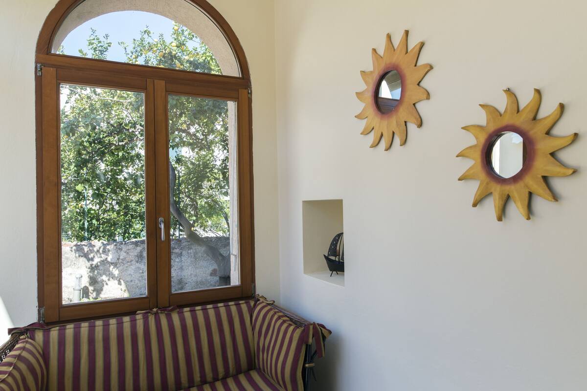 Ein Zimmer mit einem großen Bogenfenster, einem gestreiften Sofa und zwei sonnenförmigen Wandspiegeln.