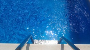 Una piscina con agua cristalina y una escalera metálica para entrar.