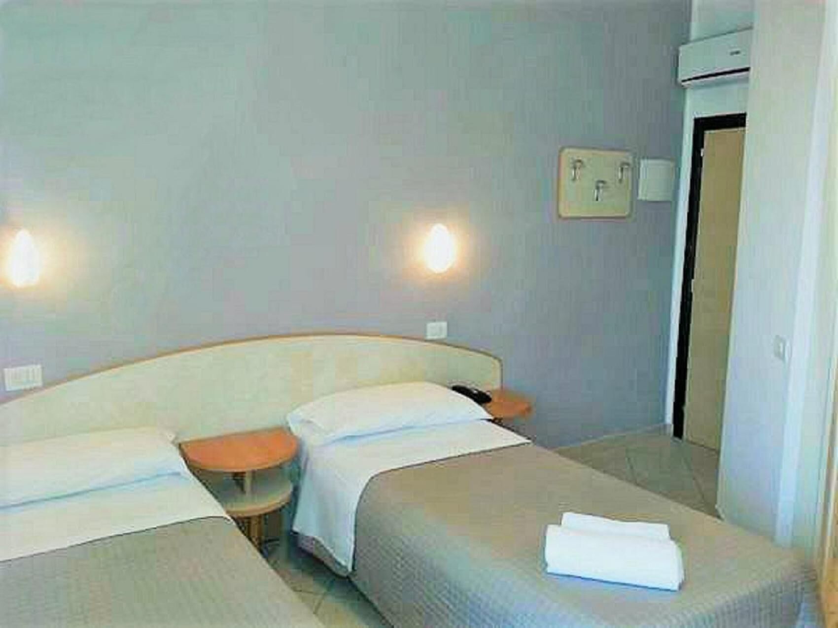 A hotel room with two beds, a bedside table, a lamp, and a door.