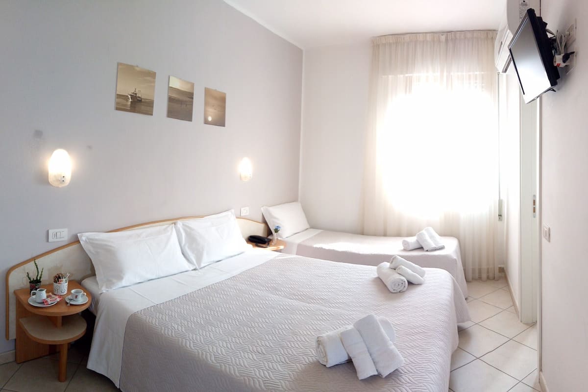 Habitación de hotel con dos camas, una mesita con una taza y una planta, y una obra de arte en la pared.