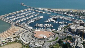 Vista aérea de un puerto deportivo con numerosas embarcaciones amarradas, una glorieta y una zona de playa.