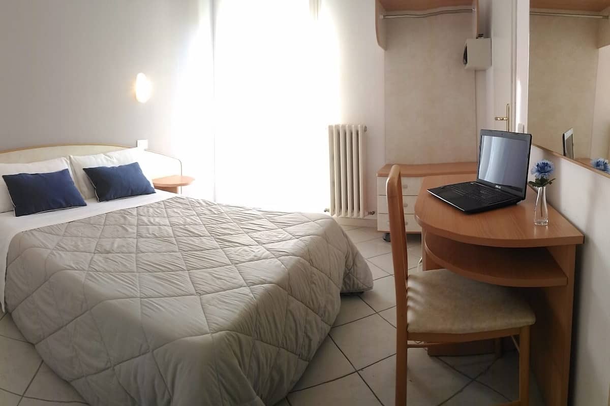 Un dormitorio con cama, mesitas de noche, un escritorio con una computadora portátil y una silla.