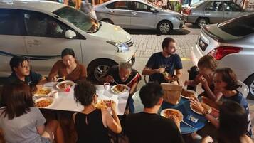 A group of people dining outdoors at a restaurant with cars parked nearby.