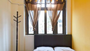 Ein Schlafzimmer mit Bett, Fenster mit Vorhängen und Kleiderständer.