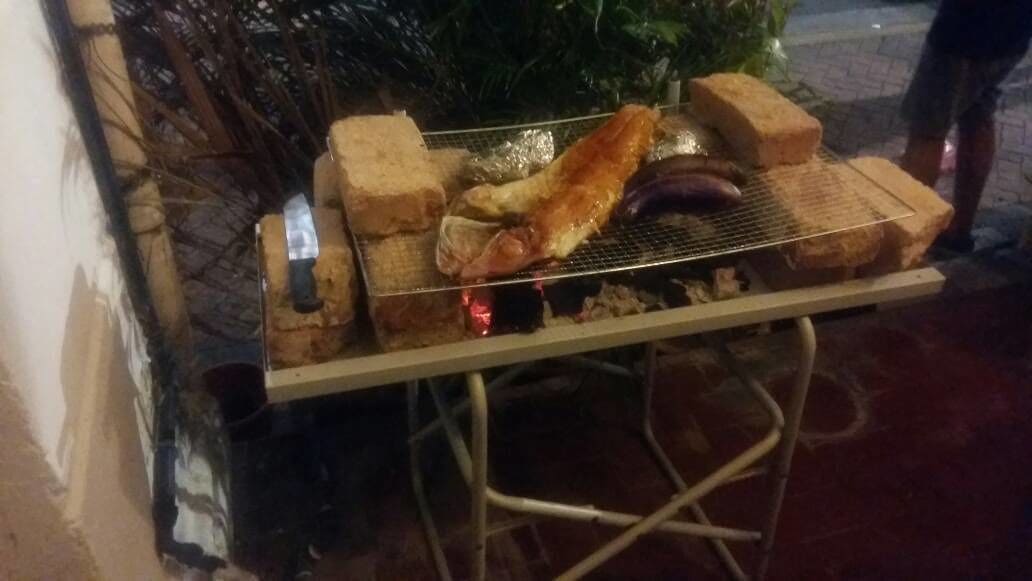 A portable grill with various meats and vegetables being cooked outdoors at night.