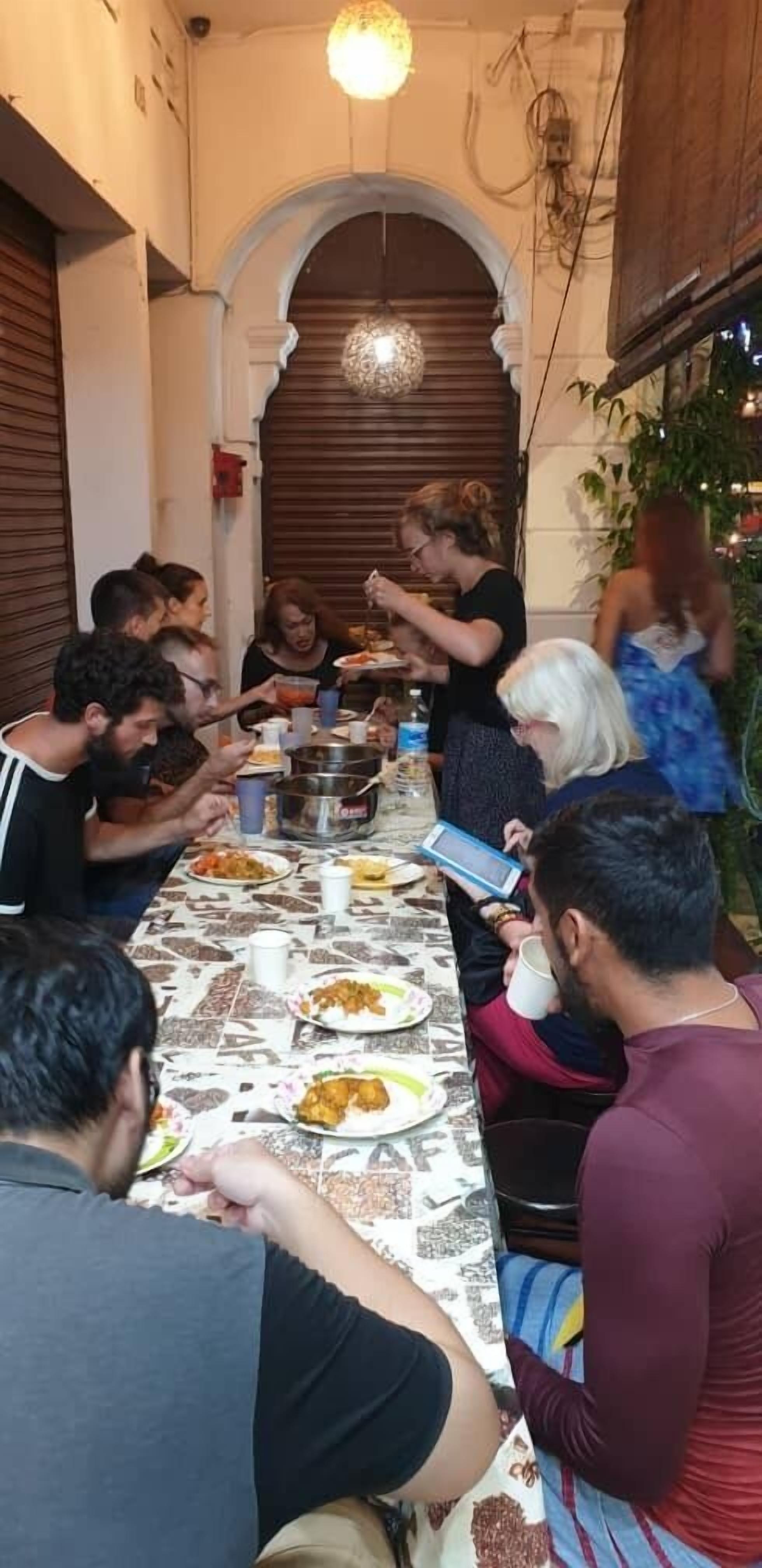 Een groep mensen dineert aan een lange tafel met diverse gerechten en drankjes.