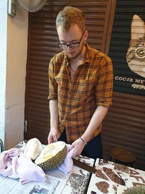A person cutting a durian fruit on a table with newspapers underneath. - Cocoa Mews Cafe & Homestay - Hostel (George Town)