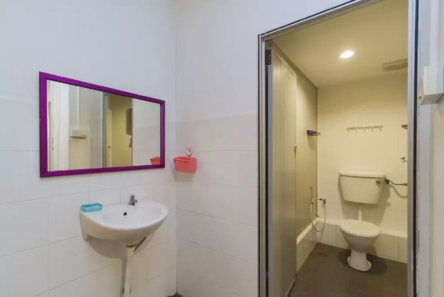 A bathroom with a white sink, a purple-framed mirror, and a toilet.