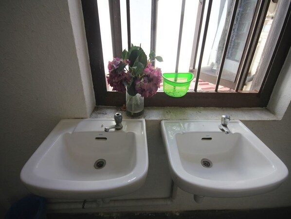Two white sinks with a window above them, a green basket, and a vase with flowers.