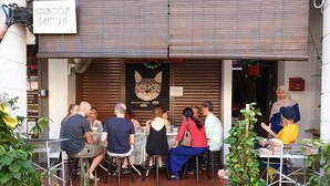 Ein Straßencafé mit Tischen und Stühlen, umgeben von Blumentöpfen.