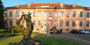 Un bâtiment imposant, doté d’une façade symétrique, de grandes fenêtres et d’un escalier central menant à l’entrée.