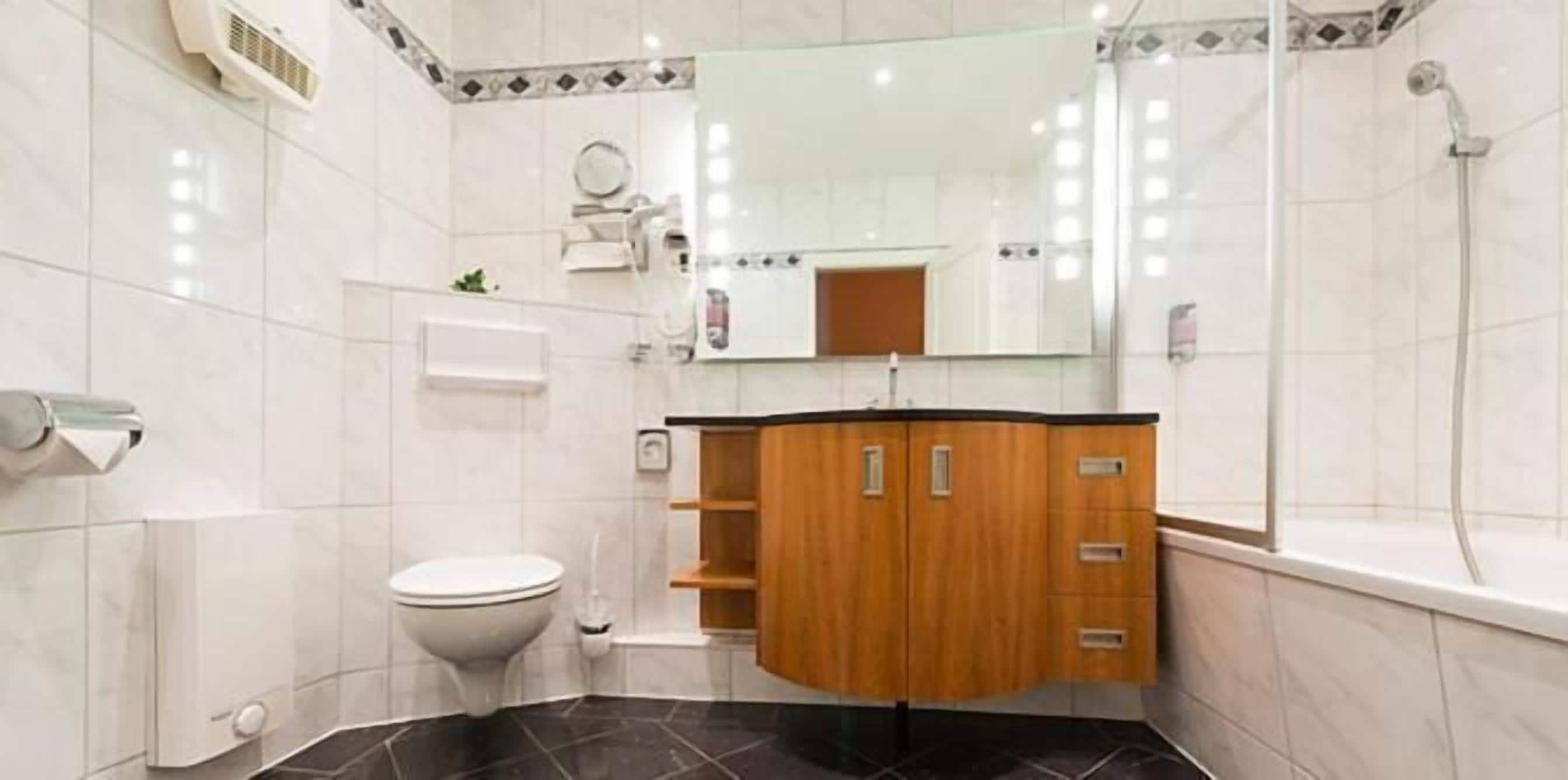 Ein modernes Badezimmer mit Toilette in Weiß, einem Holzwaschtisch mit Schubladen, einem Spiegel und einer Duschkabine.