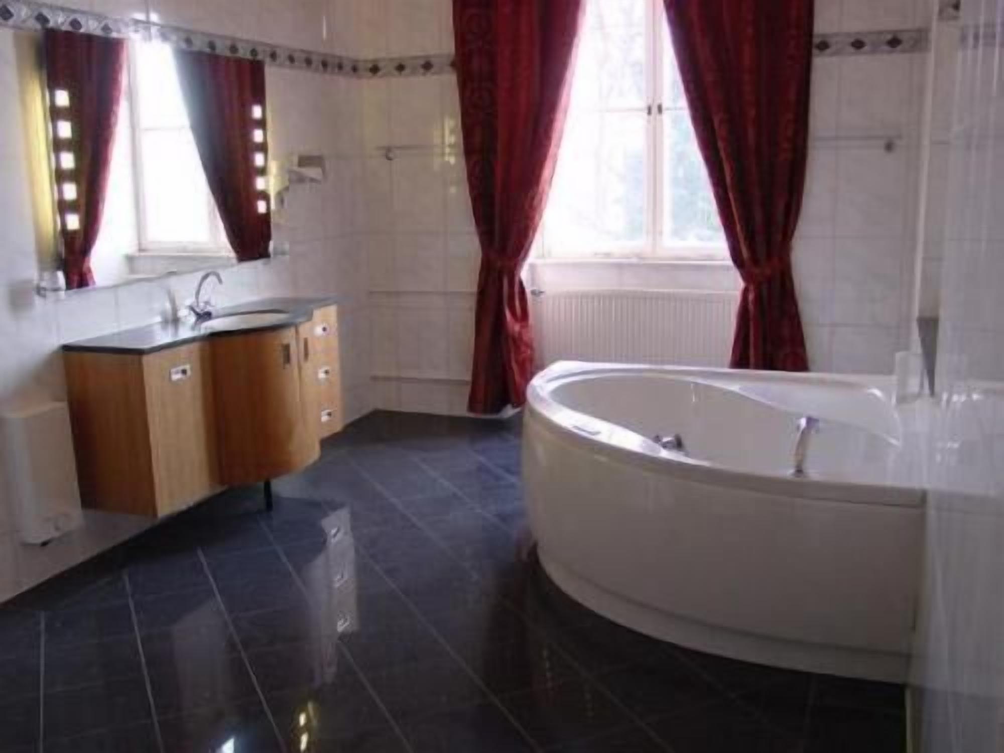 A bathroom with a bathtub, a vanity with a mirror, and red curtains.
