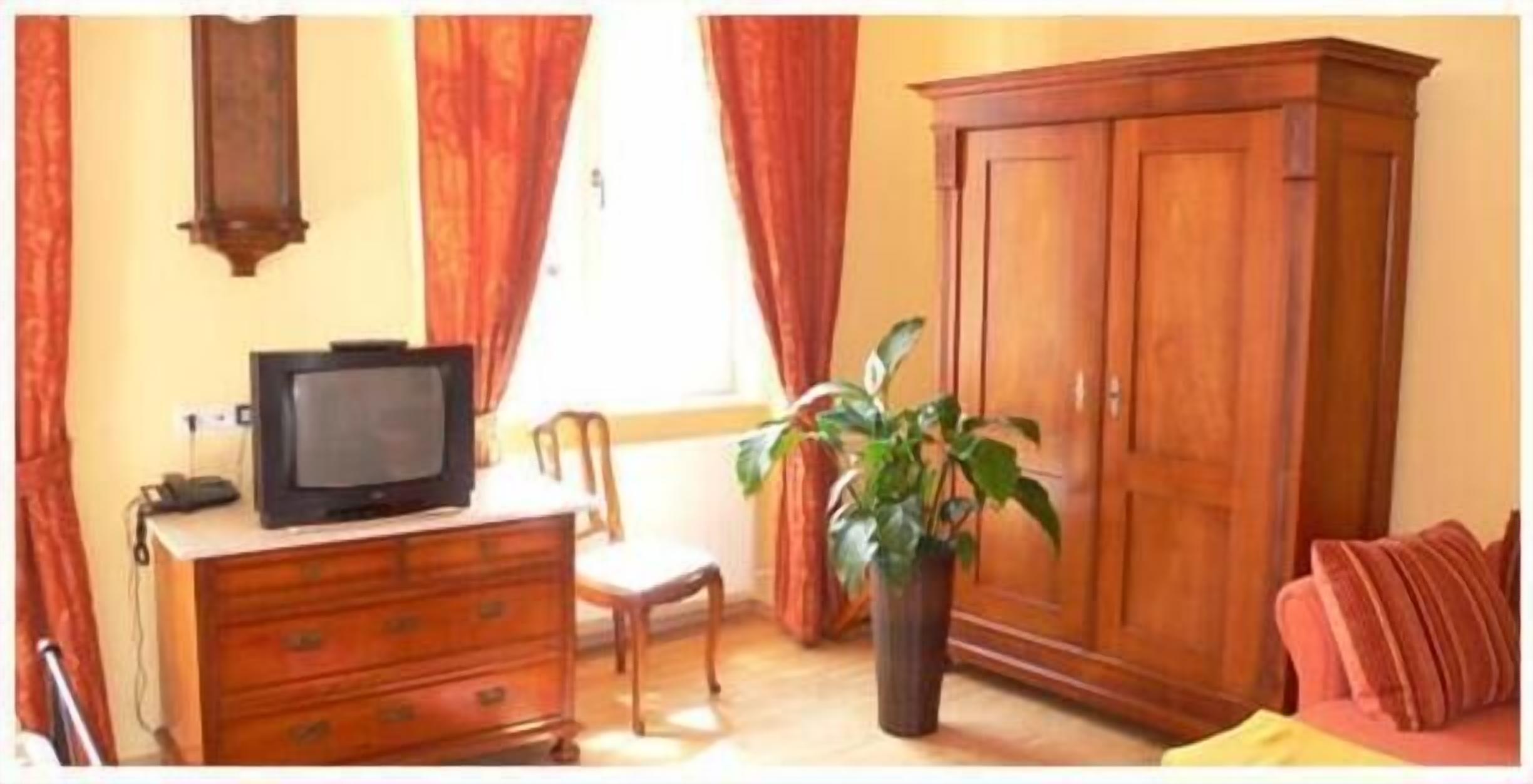 Una habitación con un aparador de madera, un televisor encima, una silla, una planta en maceta y un armario.