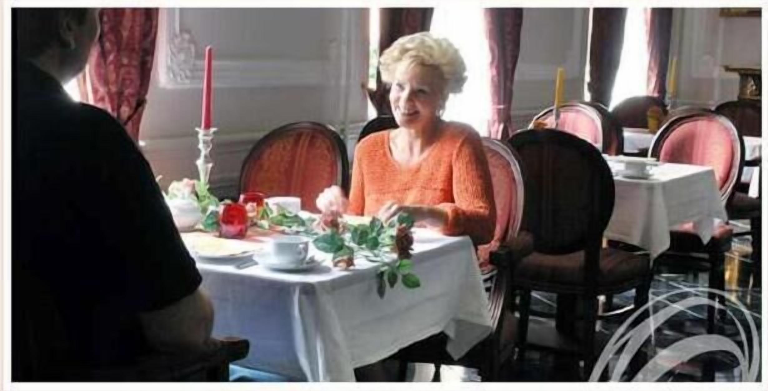 A dining area with a table set for two, featuring a white tablecloth, red candles, and a floral centerpiece.