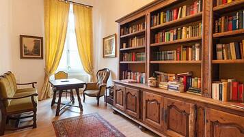 A room with a wooden bookshelf, a table, chairs, and a window with curtains.