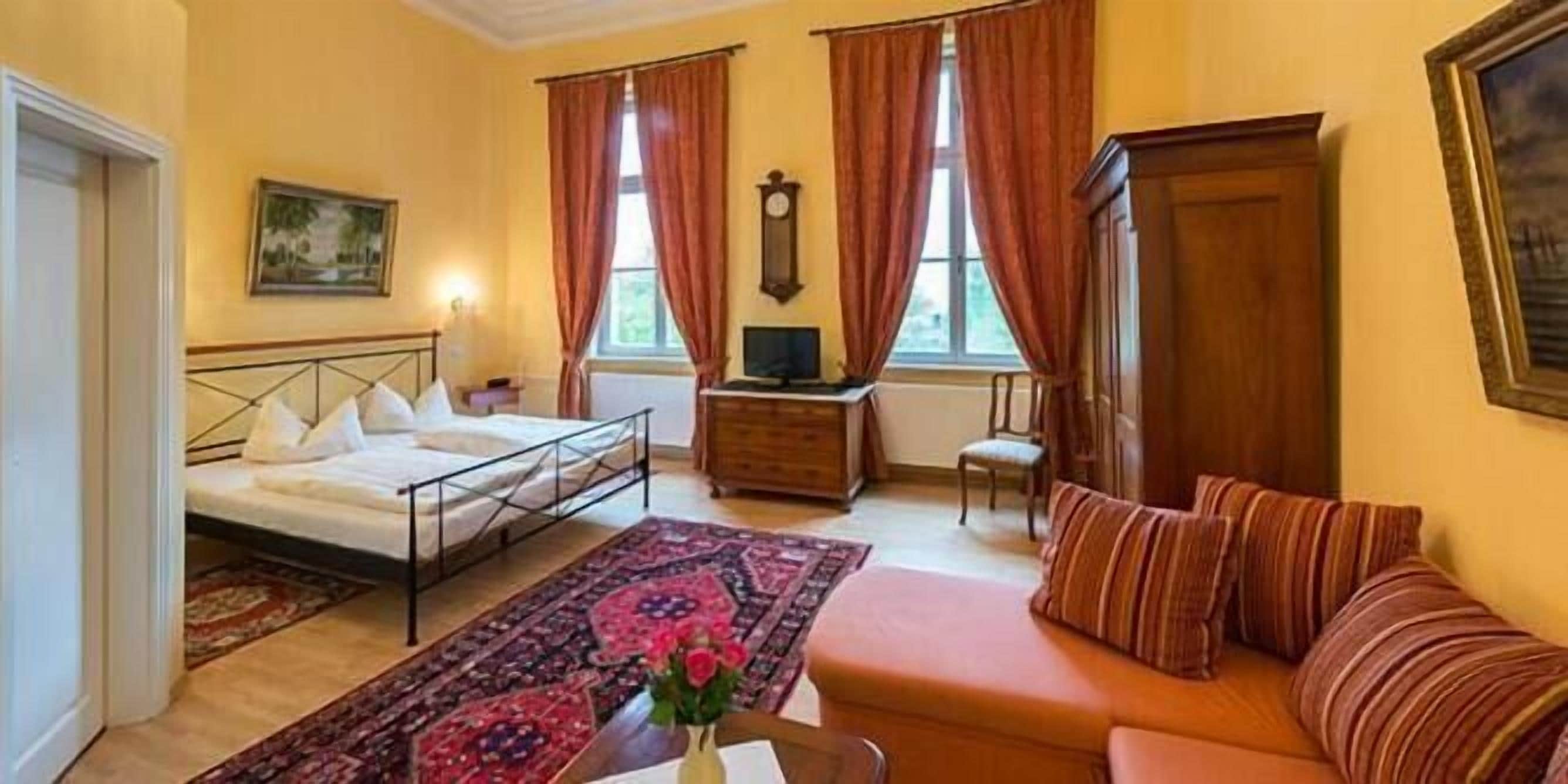A hotel room with a bed, a sofa, a TV, a wooden cabinet, and a window with curtains.