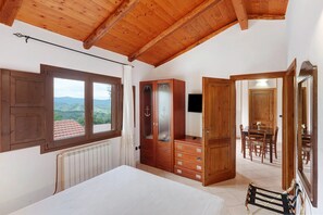 A bedroom with a wooden ceiling, a large window, a wardrobe, a bed, and a dining area with chairs and a table. - Agriturismo I Fornari (Stella Cilento)