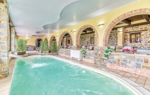 An indoor swimming pool with stone walls and arches, surrounded by potted plants and flowers. - Agriturismo I Fornari (Stella Cilento)