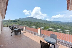 A balcony with tables and chairs, a metal railing, and a view of green hills and a mountain. - Agriturismo I Fornari (Stella Cilento)