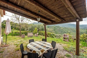A covered outdoor seating area with a table and chairs, surrounded by a wooden fence and a view of green hills. - Agriturismo I Fornari (Stella Cilento)