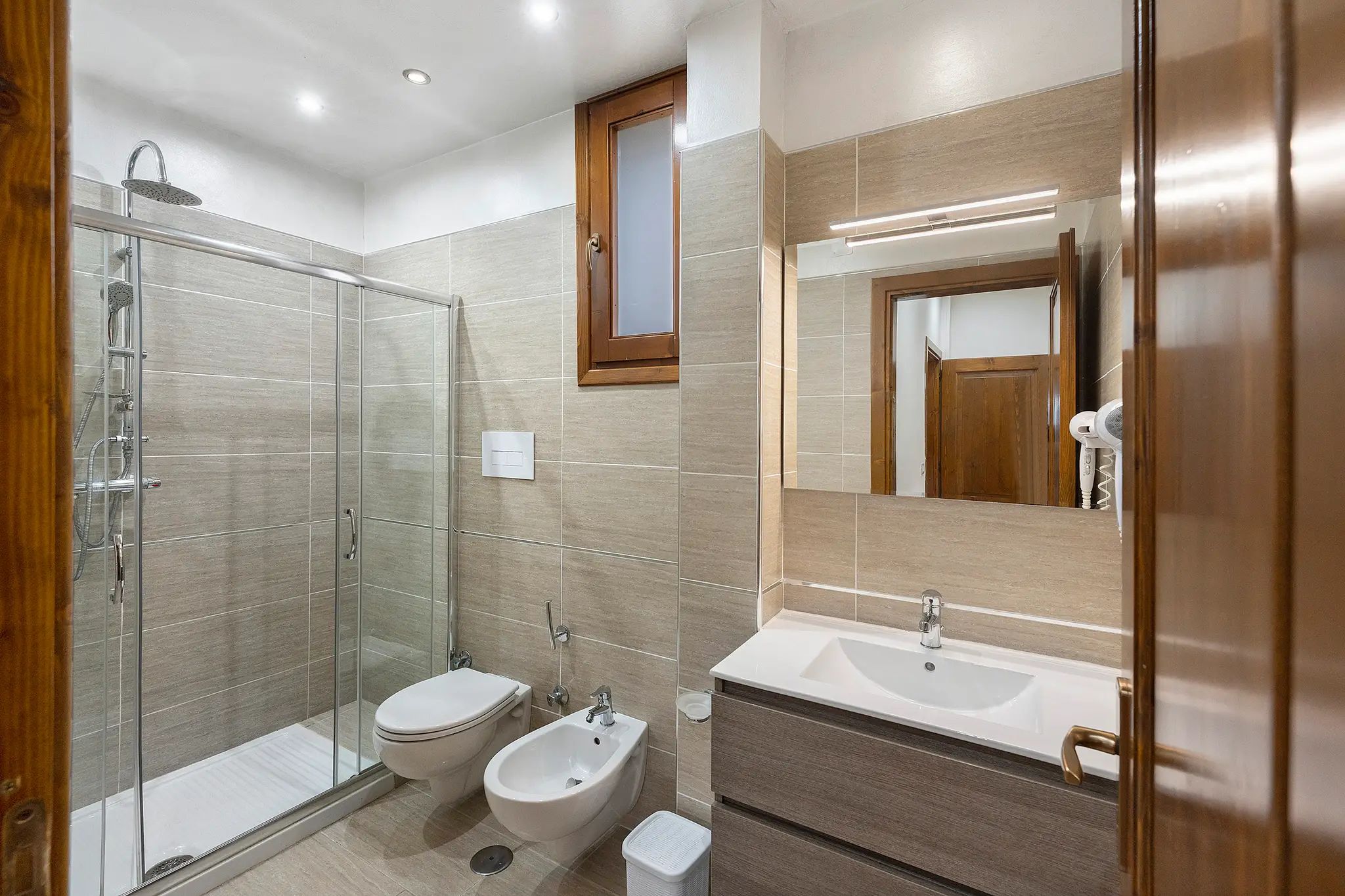 Un bagno moderno con cabina doccia in vetro, un bidet, un water e un mobile lavabo con specchio.
