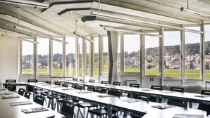 A conference room with large windows, a high ceiling with exposed beams, and a view of a town.